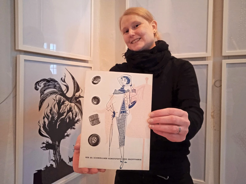 „Mehr als Schwarz und Weiß: Nackte Nymphen und scharfe Schnitte“ — Ausstellung zu Luise Neupert | Museumsmitarbeiterin Franziska Huberty mit einer von Hans und Luise Neupert gestalteten Broschüre für das VEB Schmöllner Kunststoff- und Knopffabrik aus der Sammlung des Museums Burg Posterstein. 